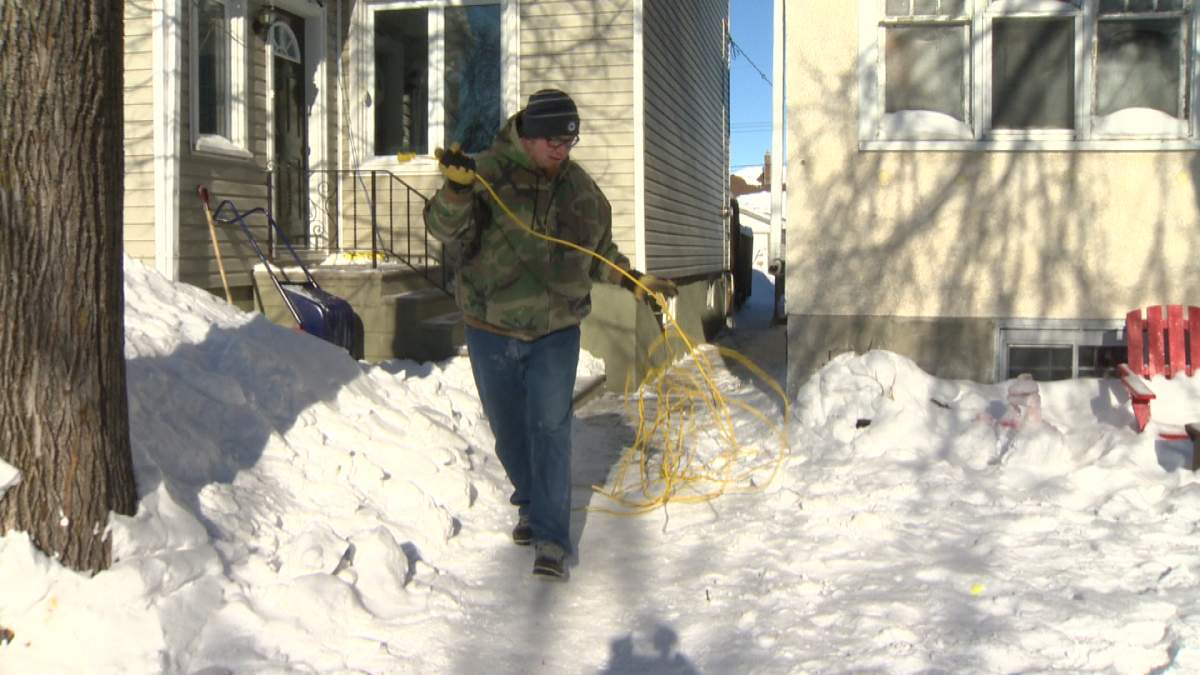 Paul Peters stretches his extension cord from his home, across the sidewalk and to his vehicle parked on College Avenue in Winnipeg on Wednesday.