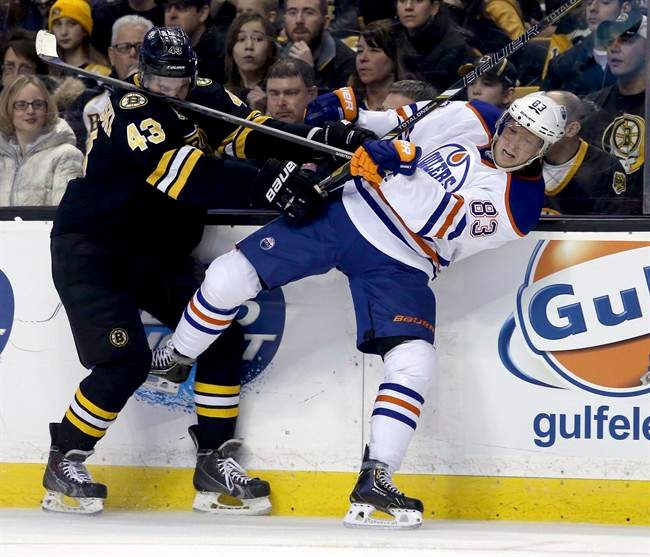 Boston Bruins defenceman Matt Bartkowski (43) takes a stick in the face as he checks Edmonton Oilers right wing Ales Hemsky (83), of the Czech Republic, into the boards during the second period of an NHL hockey game, Saturday, Feb. 1, 2014 in Boston. 