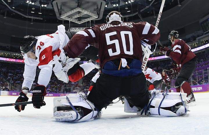 Canada forward Corey Perry trips over Latvia goaltender Kristers Gudlevskis in the first period of a men’s ice hockey game at the 2014 Winter Olympics, Wednesday, Feb. 19, 2014, in Sochi, Russia. (AP Photo/Julio Cortez)