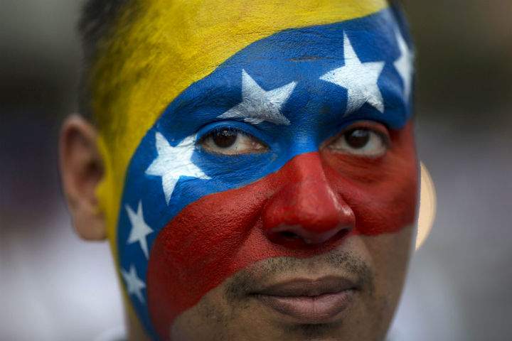 David Aranguren, his face painted with a representation of Venezuela's national flag, poses for a photo during an anti-government demonstration in Caracas, Venezuela, Saturday, Feb. 22, 2014. Supporters and opponents of the government of President Nicolas Maduro are holding competing rallies in the bitterly divided country.