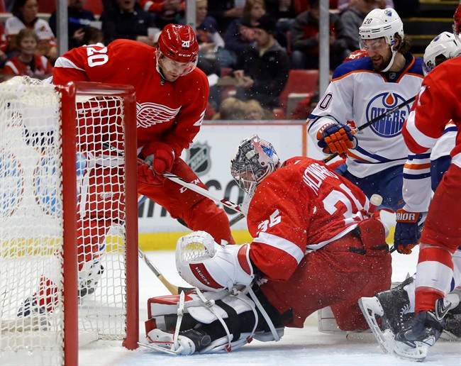 Detroit Red Wings goalie Jimmy Howard (35) stops a shot during a scrum at the net against Edmonton Oilers' Luke Gazdic, right, as Detroit Red Wings' Drew Miller, left, helps defend during the first period of an NHL hockey game Friday, March 14, 2014, in Detroit.