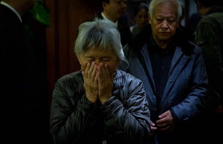 An elderly woman, one of the relatives of Chinese passengers aboard missing Malaysia Airlines Flight MH370, covers her face out of frustration as she leaves the hotel ballroom.