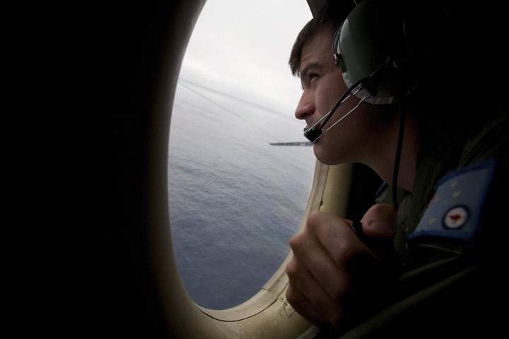 In this Monday, March 24, 2014 photo, a crewman of an RAAF AP-3C Orion aircraft looks out his observation window whilst searching for missing Malaysia Airlines Flight MH370 over the Indian Ocean. 