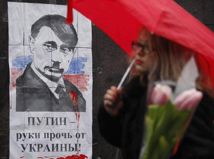 A woman walks in front of poster depicting Russian President Vladimir Putin as Adolf Hitler and signed "Hands off  Ukraine" in Kiev on March 3, 2014.  Yury Kirnichny/AFP/Getty Images.
