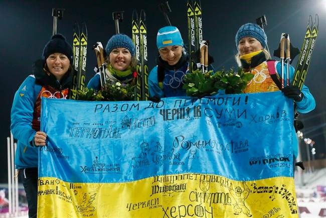FILE - In this Friday, Feb. 21, 2014, file photo Ukraine's relay team Vita Semerenko, Juliya Dzhyma, Olena Pidhrushna and Valj Semerenko, from left, celebrate with a Ukrainian flag with writings on it after winning the gold during the women's biathlon 4x6k relay, at the 2014 Winter Olympics in Krasnaya Polyana, Russia.