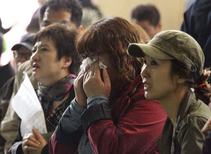 A mother weeps as she and others search for their children’s names among a list of survivors.
