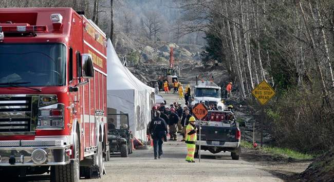 Emergency personnel stage on Highway 530 as work to clear debris from the roadway left behind from a deadly mudslide continues behind, Wednesday, April 2, 2014, in Oso, Wash. 