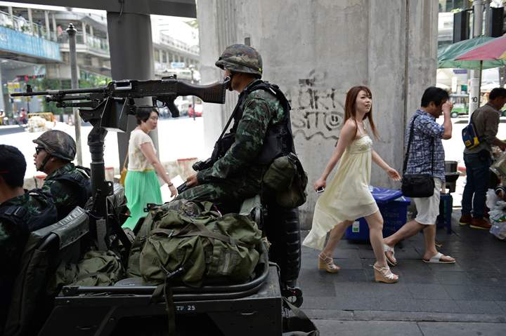 People walk past Thai army soldiers sitting in a jeep mounted with a machine gun as they secure a main intersection in Bangkok on May 20, 2014. 