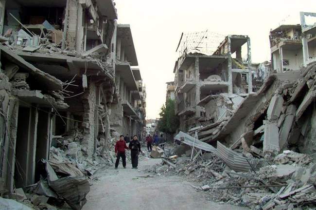 his file photo released on Thursday Nov. 29, 2012 by the anti-government activist group Homs City Union of The Syrian Revolution, which has been authenticated based on its contents and other AP reporting, shows Syrian citizens walking in a destroyed street that was attacked by Syrian forces warplanes, at Abu al-Hol street in Homs province, Syria. A protest is being held in Montreal to commemorate the fifth anniversary of the revolution. Sunday, March 13, 2016.