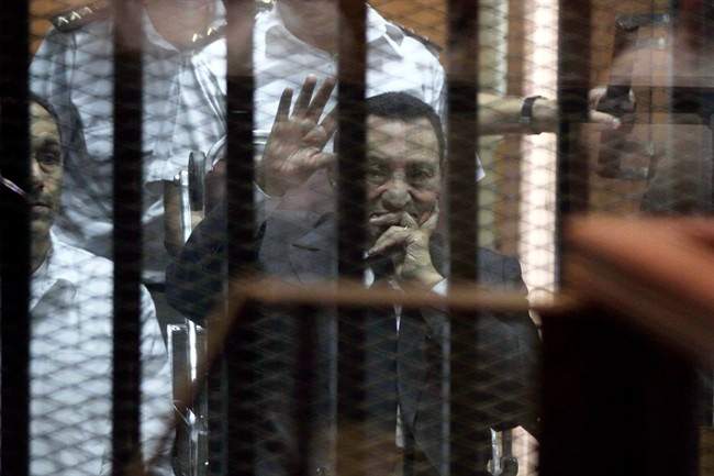 Ousted Egyptian President Hosni Mubarak, sitting in a defendants cage, waves during a court hearing as his son Gamal, left, in Cairo, Egypt, Wednesday, May 21, 2014. 
