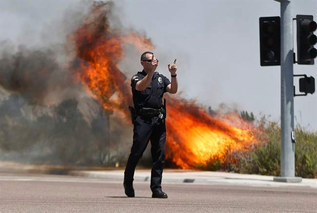 A Carlsbad,Calif. police officer turns traffic away as flames leap behind him Wednesday, May 14, 2014, in Carlsbad, Calif.