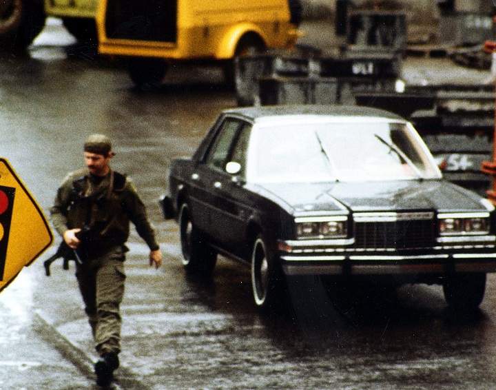A member of the SWAT team runs with the car carrying the gunman that shot and killed three people and injured 13 others at the Quebec National Assembly building in Quebec City on May 8, 1984.