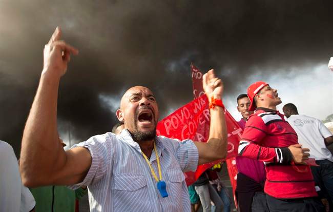 Members of the Homeless Workers Movement protest against the money spent on the World Cup near Itaquerao stadium which will host the international soccer tournament's first match in Sao Paulo, Brazil, Thursday, May 15, 2014. Brazilians are angry at the billions spent to host the World Cup, much of it on 12 ornate football stadiums, one-third of which critics say will see little use after the big event. The smoke behind comes from burning tires. (AP Photo/Andre Penner)