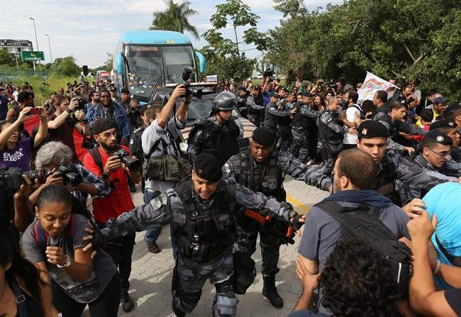 Riot police try to keep demonstrators away from the bus carrying some members of Brazil's national soccer team departing for the Granja Comary training center, where the team will stay during the World Cup, in Rio de Janeiro, Brazil, Monday, May 26, 2014. Demonstrators are protesting against the money being spent by the local government on the World Cup. (AP Photo/Leo Correa)