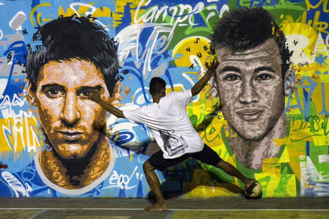 Youngsters play football in front of a mural of Argentine football player Lionel Messi (L) and Brazil's player Neymar da Silva Santos Junior at a field of Tavares Bastos shantytown (favela) in Rio de Janeiro, Brazil on June 8, 2014, just four days ahead of the FIFA World Cup 2014. AFP PHOTO / YASUYOSHI CHIBA (Photo credit should read YASUYOSHI CHIBA/AFP/Getty Images)