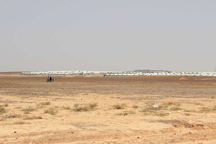 A family walks through Azraq Camp, with shelters in the distance