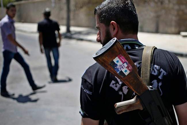 This Aug. 21, 2013 file photo shows a Syrian military soldier holding his AK-47 with a sticker of Syrian President Bashar Assad and Arabic that reads, "Syria is fine," as he stands guard at a check point in Damascus, Syria. 
