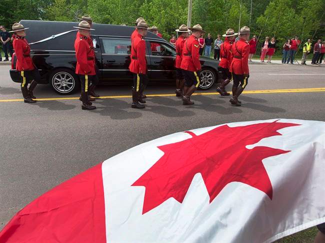 Onlookers wave a Canadian flag during the funeral procession for the three RCMP officers who were killed in the line of duty in Moncton, N.B. on Tuesday, June 10, 2014. 