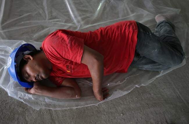 In this Sunday, June 15, 2014 photo, a labourer sleeps with his hard hat on during his midday break at a construction site in Dubai, United Arab Emirates. A midday work ban goes into effect across the United Arab Emirates for construction workers and outdoor labourers to protect them from the risks of direct sunlight and extremely high temperatures during the hottest summer months.