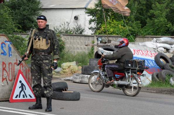 A motorcyclist drives by a pro-Russian militant standing guard at a checkpoint on the road between Lugansk and Donetsk, eastern Ukraine, on July 9, 2014. 