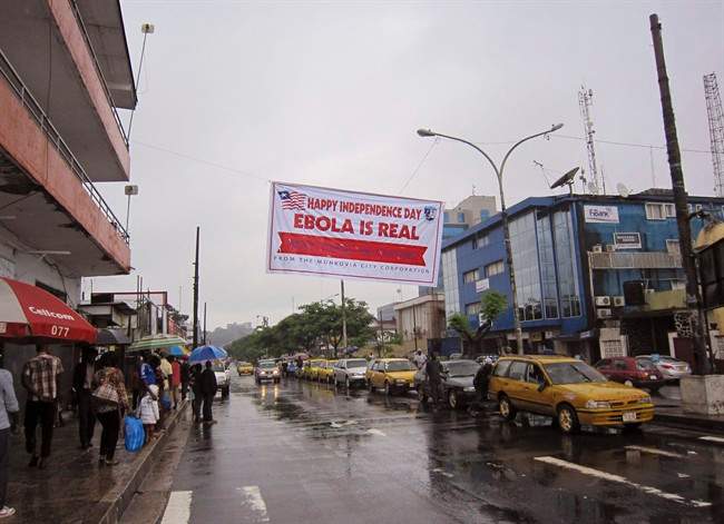 In this photo taken on Monday, July 28, 2014, people hang out in a street under a banner which warns people to be cautious about Ebola, in Monrovia, Liberia. 