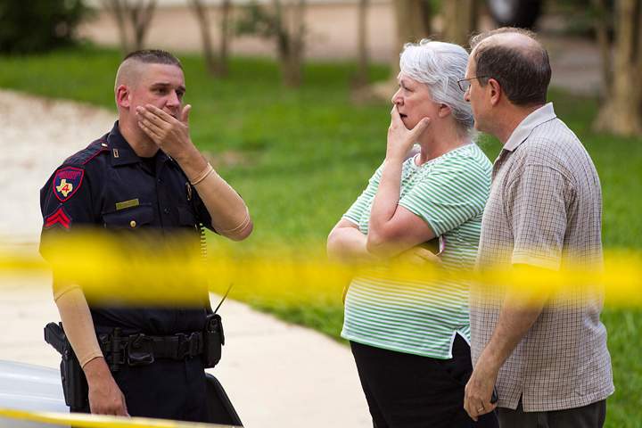 People stand with a law enforcement officer near the scene of a shooting Wednesday, July 9, 2014, in Spring, Texas.