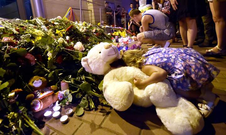 A young girl places her head on a teddy bear as people light candles and place flowers in front of the Embassy of the Netherlands in Kiev.