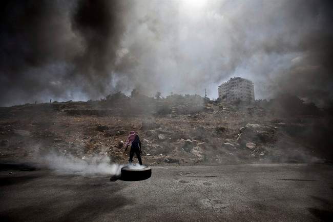 A Palestinian man burns a tire during clashes with Israeli soldiers following a protest against the Israeli offensive in Gaza, outside Ofer, an Israeli military prison near the West Bank city of Ramallah, Friday, July 18, 2014.