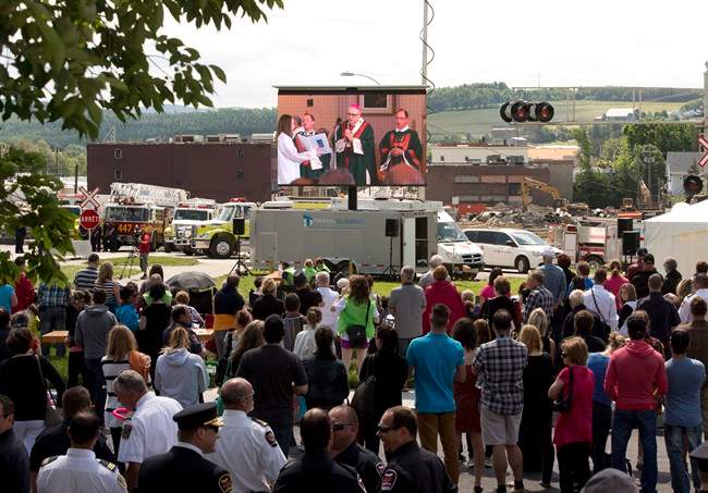 People watch the mass outside the church on a screen overlooking downtown Sunday, July 6, 2014 in Lac-Megantic, Que.