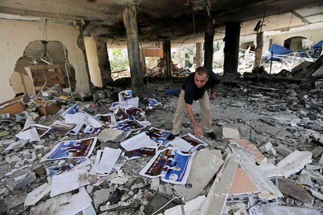 A Palestinian searches the rubble of a center for disabled, that is littered with posters soliciting donations to support the Al Mabara association for handicapped run by Hamas, after an Israeli missile strike in Beit Lahiya, in the northern Gaza Strip, Saturday, July 12, 2014.