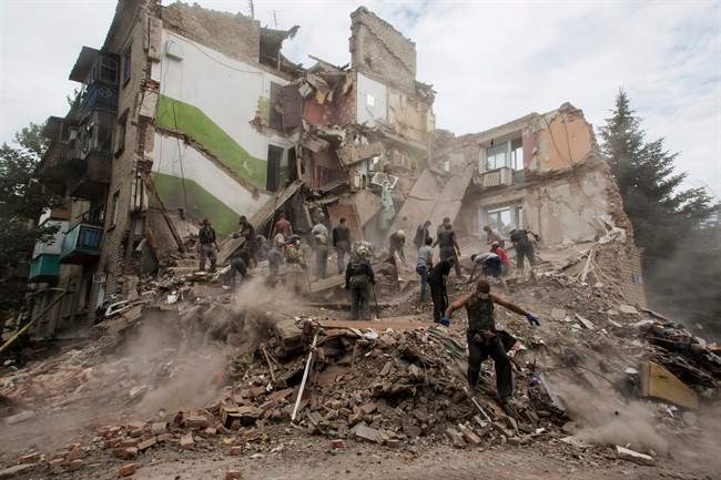 A man walks in a bomb crater near a damaged private house after an airstrike in Snizhne, 100 kms east from the city of Donetsk, eastern Ukraine Tuesday, July 15, 2014. An airstrike demolished an apartment block in eastern Ukraine on Tuesday, killing at least 11 civilians, rescue workers said. 