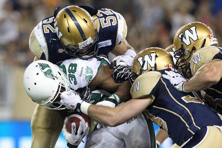 Louie Richardson (#52) of the Winnipeg Blue Bombers stops Tristan Jackson (#38) of the Saskatchewan Roughriders during a CFL game in 2014.