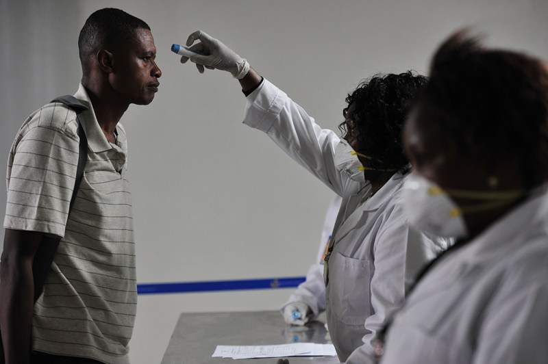 Kenyan health officials take passengers temperature as they arrive at the Jommo Kenyatta International Airport (JKIA) on August 14, 2014 in Nairobi. AFP PHOTO / SIMON MAINA .