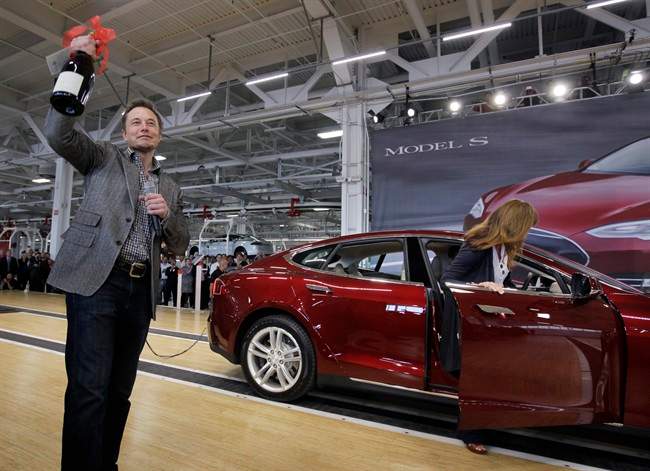 In this June 22, 2012 file photo, Tesla Motors Inc. CEO Elon Musk holds up a bottle of wine given as a gift from one of their first customers, right, during a rally at the Tesla factory in Fremont, Calif.