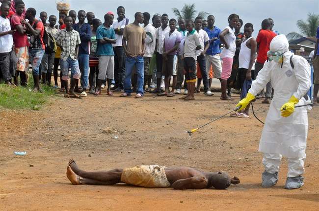 A health worker, right, sprays a man with disinfectant chemicals as he is suspected of dying due to the Ebola virus as people, rear, look on in Monrovia, Liberia, Thursday, Sept. 4, 2014. 