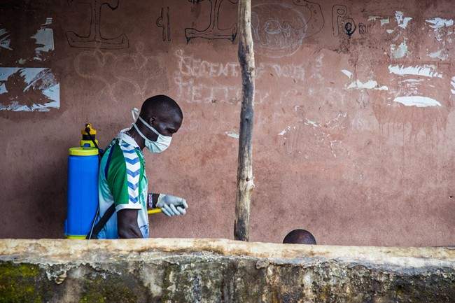 A health worker, left, sprays disinfectant around the area where a man, right, suspected of suffering from the Ebola virus, sits with a part of his head visible, before loading him into an ambulance in Freetown, Sierra Leone, Wednesday, Sept. 24, 2014.