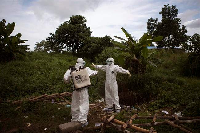 In this photo taken on Wednesday, Sept. 24, 2014, healthcare workers spray each other with disinfectant after working inside a morgue with people suspecting of dying from the Ebola virus, in Kenema, Sierra Leone, Thursday, Sept. 25, 2014. 