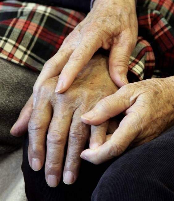 A care giver holds the hand of her husband, an Alzheimer's patient.