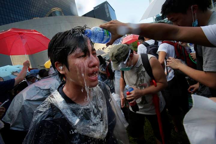 A student protester is overcome by pepper spray from riot police as thousands of protesters surround the government headquarters in Hong Kong Sunday, Sept. 28, 2014.