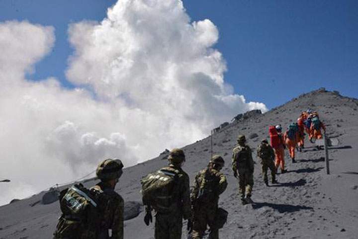 In this photo taken Sunday, Sept. 28, 2014 and released by the Japan Ground Self-Defense Force (JGSDF), JGSDF personnel and fire fighters head for the summit of Mount Ontake to rescue people who have been trapped in the mountaintop lodge during the eruption as plumes of gas and ash are spewed out, one day after the volcano became active in central Japan.