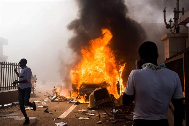 In this photo taken Thursday, Oct. 30, 2014, a car burns after being set alight by protesters outside the parliament building in Burkina Faso as people protest against their longtime President Blaise Compaore who seeks another term, in Ouagadougou, Burkina Faso. 