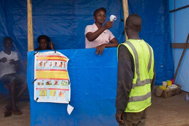 In this photo taken on Tuesday, Oct. 21, 2014, a health worker takes the temperature of a man, right, as part of the countries fight against the spread of the Ebola virus, on the Masiaka Highway, forming part of a trans-West African highway, which links all West African States, on the outskirts of the capital city of Conakry, Guinea.