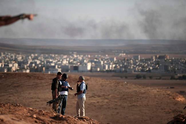 Members of the media talk with a Turkish soldier, left, on a hilltop on the outskirts of Suaruc, at the Turkey-Syria border, overlooking Kobani, Syria, background, during fighting between Syrian Kurds and the militants of Islamic State group, Wedesday, Oct. 15, 2014. 