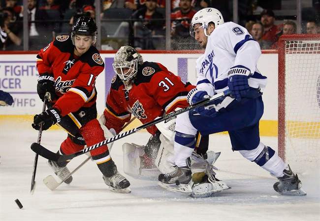 Tampa Bay Lightning Tyler Johnson, right, fights for the puck as Calgary Flames Johnny Gaudreau, left, swats it away while goalie Karri Ramo, from Finland, looks on during second period NHL hockey action in Calgary, Tuesday, Oct. 21, 2014.