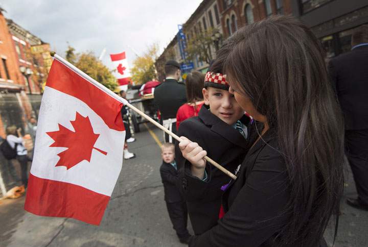 Marcus Cirillo, 5, the son of Nathan Cirillo, accompanied by his aunt, Natasha Cirillo, holds a flag during a short pause as the body of Nathan Cirillo is escorted through the streets toward his funeral service in Hamilton, Ont., on Tuesday, October 28, 2014. THE CANADIAN PRESS/Peter Power