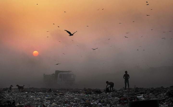 A thick blanket of smoke is seen against the setting sun as young ragpickers search for reusable material at a garbage dump in New Delhi, India, Friday, Oct. 17, 2014. The WHO says that 1.7 million children die every year due to polluted environments.