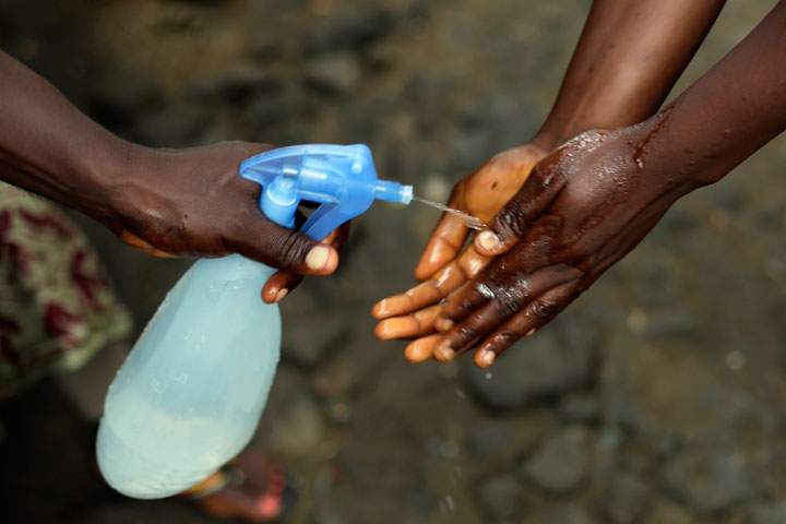 In this photo taken on Thursday Oct. 2, 2014, Promise Cooper, 16, has her hands cleaned with a chlorine solution by Kanyean Molton Farley, a community activist who visits Promise and her two brothers, Emmanuel Junior, 11, and Benson, 15, on a daily basis at their St. Paul Bridge home in Monrovia, Liberia. The Cooper children are now orphans, having lost their mother Princess in July, and their father Emmanuel in August. Their 5-month-old baby brother Success also succumbed to the virus in August.