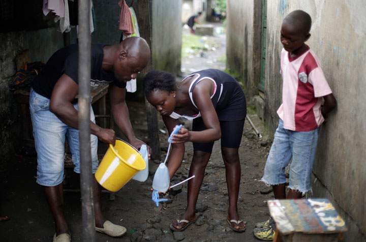 In this photo taken Thursday Oct. 2, 2014, Promise Cooper, 16, fills a bottle with a chlorine solution with the help of Kanyean Molton Farley, a community activist who visits Promise and her two brothers, Emmanuel Junior, 11, right, and Benson, 15, not pictured, on a daily basis at their St. Paul Bridge home in Monrovia, Liberia.