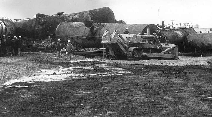 An earth mover lays a road of gravel at the derailment site in preparation for equipment to be brought in to work on a tank at right containing propane. Tank has to be turned over for the openings to be reached. At midnight Saturday, Nov 11, 1979, a derailment of a CP Rail freight train and subsequent explosion resulted in a highly toxic chlorine gas leak from a ruptured tanker car.