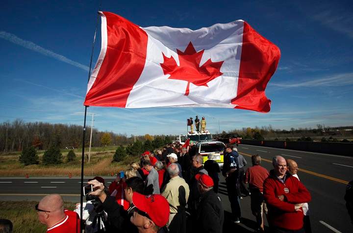 Crowds wave Canadian flags on an overpass at the Veterans Memorial Highway waiting for a procession transporting the body of Cpl. Nathan Cirillo to pass by in Ottawa on Friday, October 24, 2014.